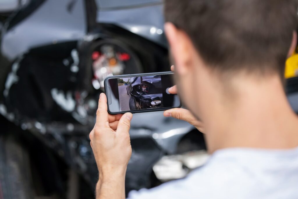 Person taking a photo of a damaged car with a smartphone.