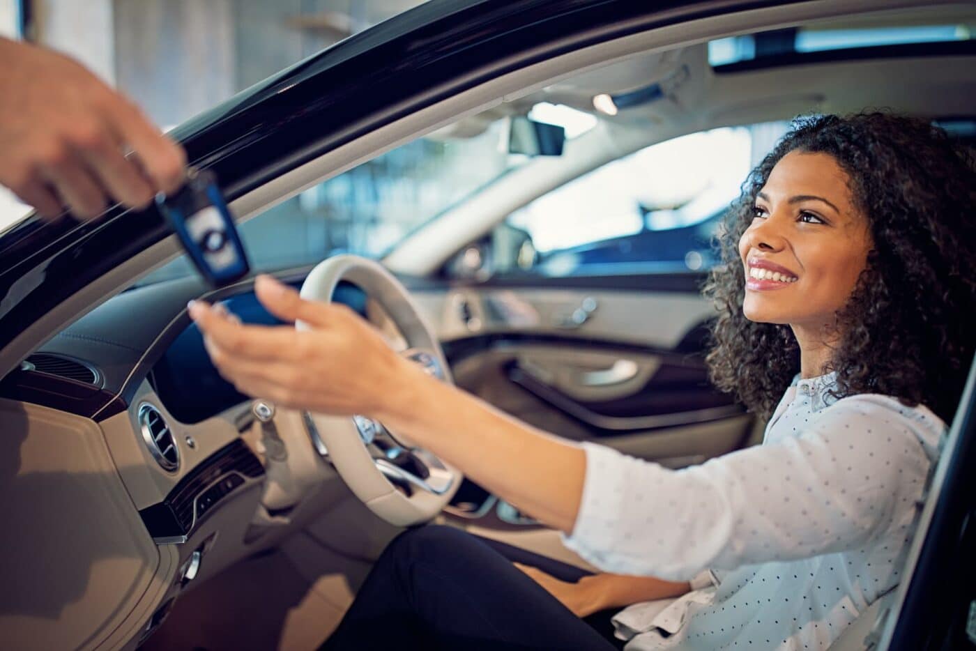 Woman in a car receiving keys from another person on the driver's-side.